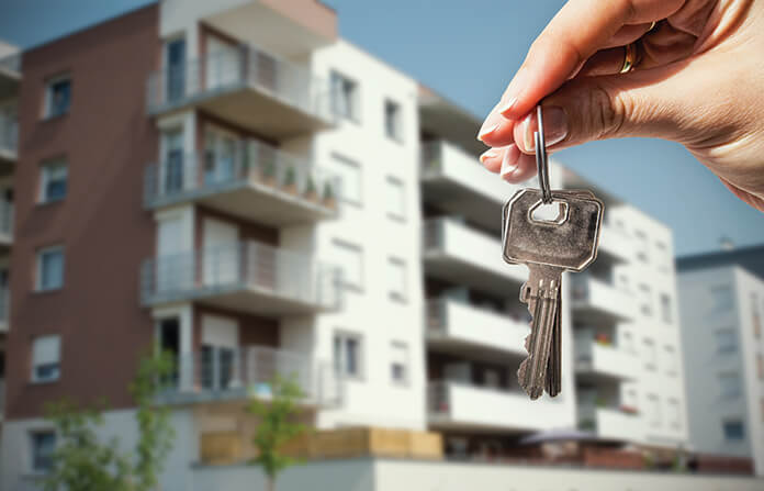 A hand holding a set of house keys in front of an apartment block